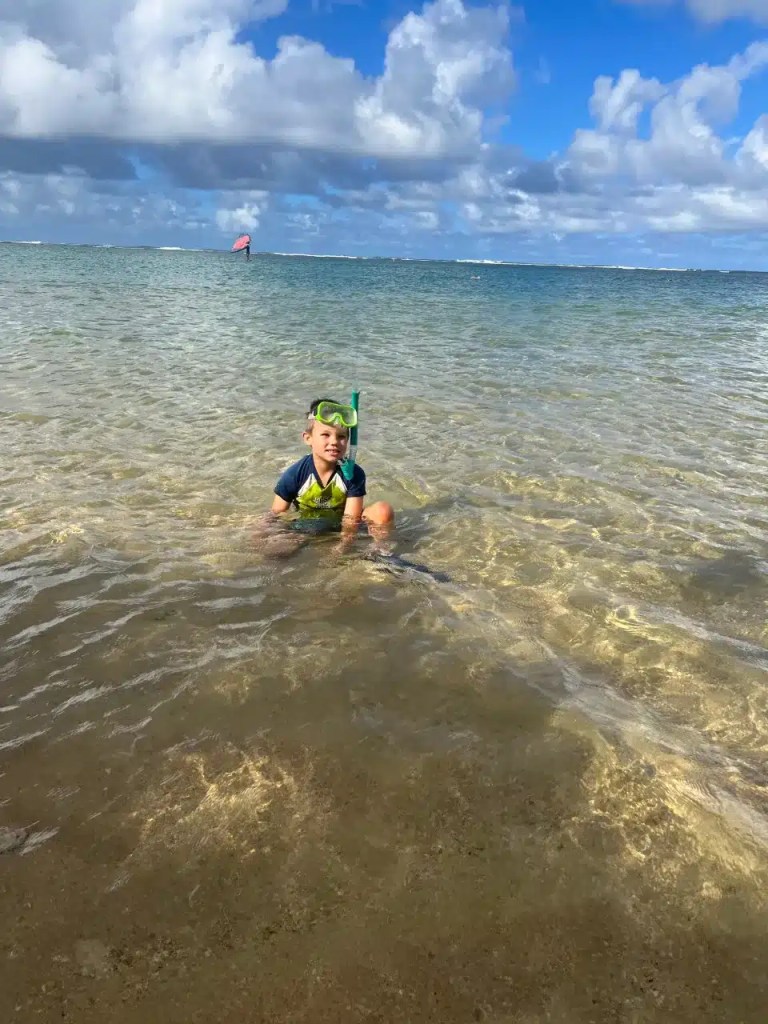 A kid in the crystal clear water at one of the Hawaii Kauai beaches that's perfect for snorkeling.