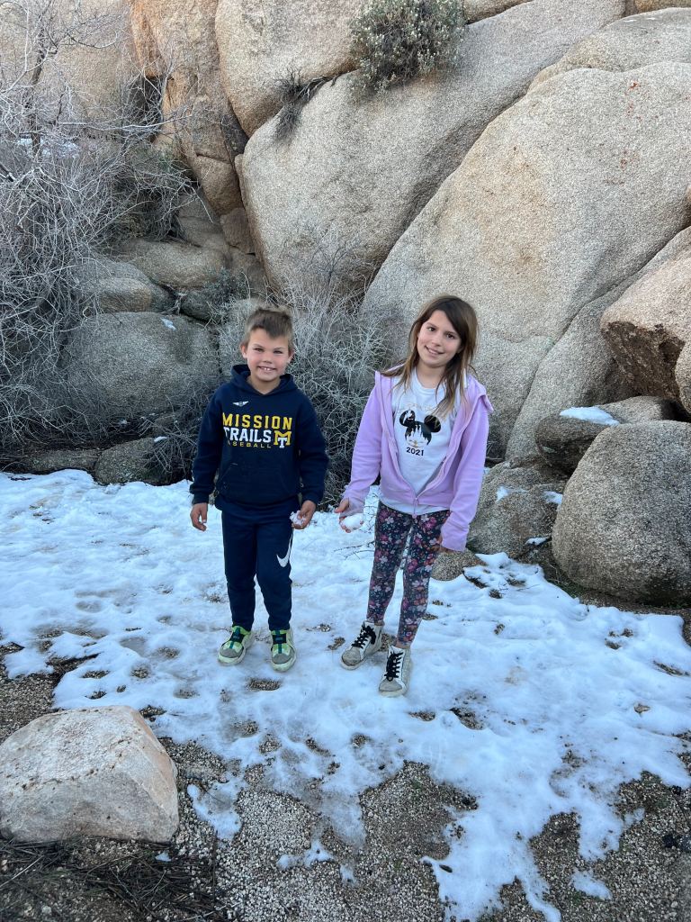 Two kids standing in snow while RV camping in Joshua Tree