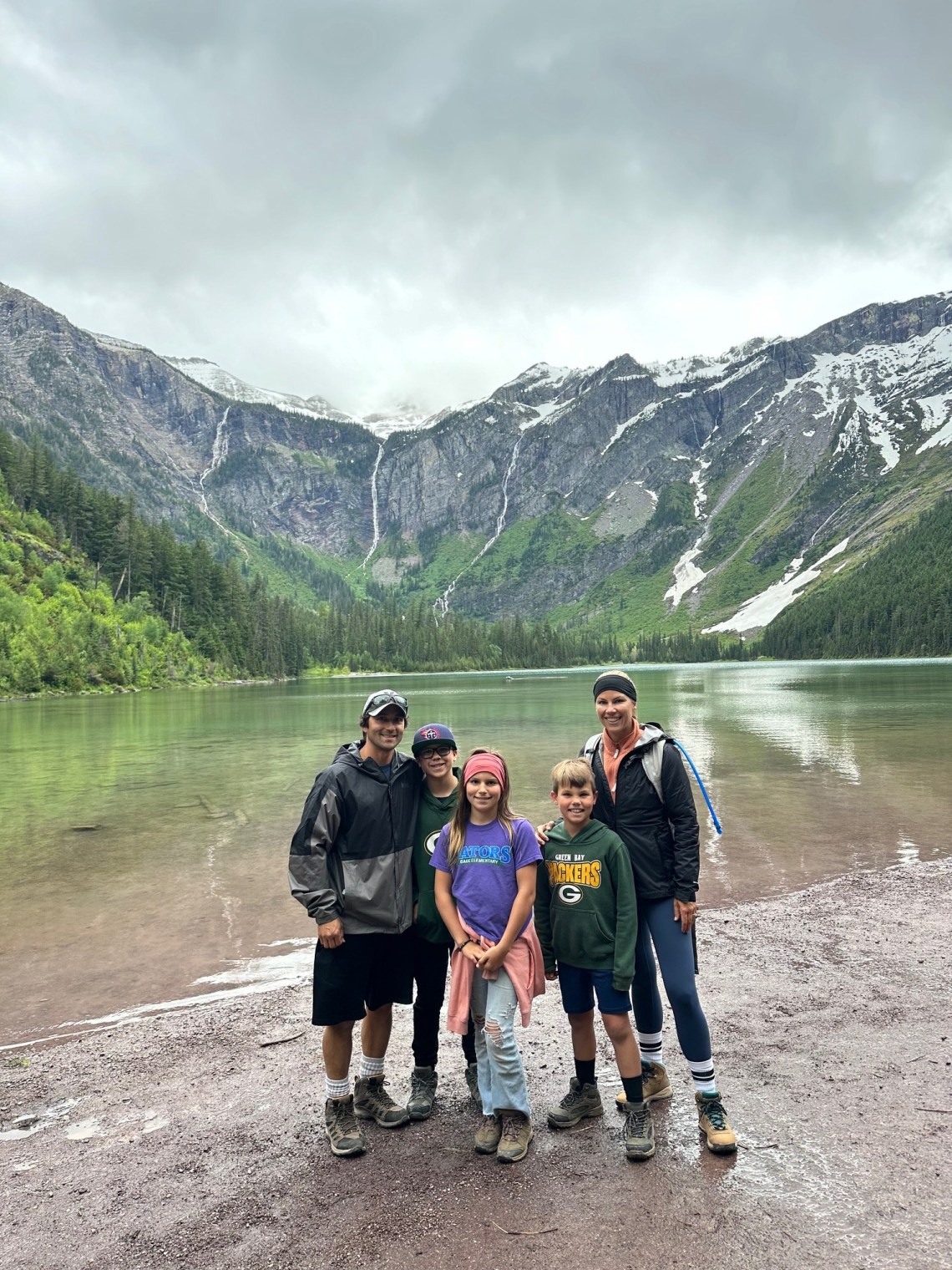 A family of five posing by Lake Avalanche in Glacier National Park with a large snow-streaked mountain in the background