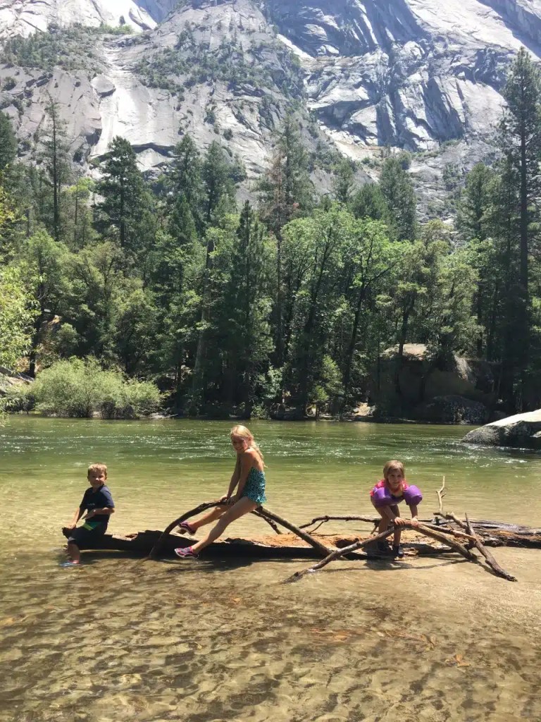 Three kids sitting on a tree branch in Mirror Lake in Yosemite