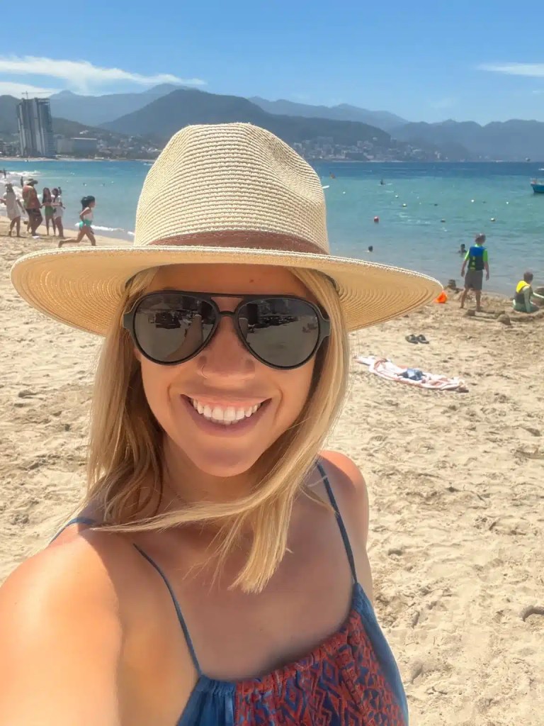 A woman in a straw hat with sunglasses and a sundress at the beach in one of the best Mexico cities to vacation in.