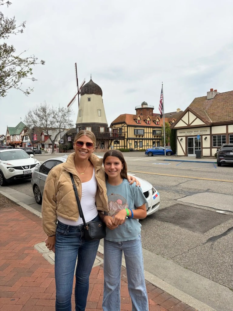 img_9234 A woman and girl posing together on a street in Solvang, California, with a large windmill and a United States Post Office in the background.