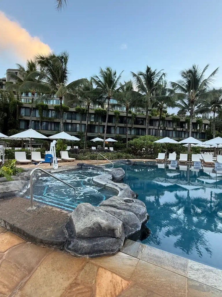 View of a swimming pool with a hot tub surrounded by palm trees and lounge chairs at the 1 Hotel Hanalei Bay Resort.