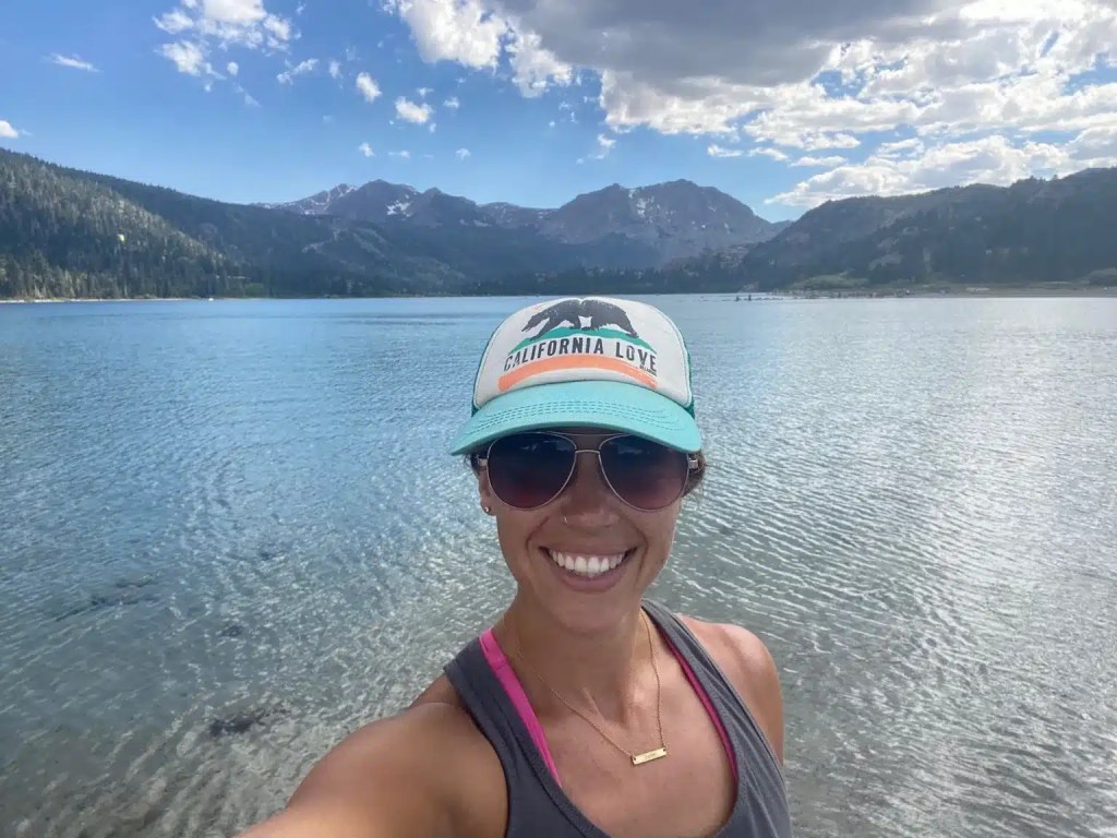 A person smiling by a lake in Mammoth Lakes, California, with mountains in the background and a clear sky.