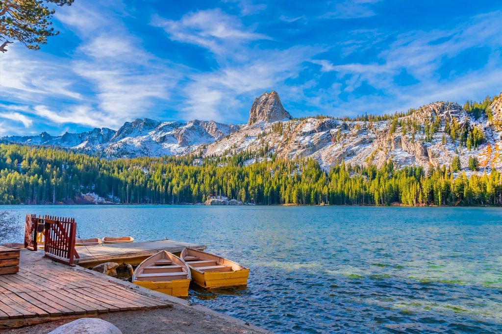 Scenic view of a lake surrounded by mountains and forests, showcasing blue water, a wooden dock, and yellow boats at the shore.