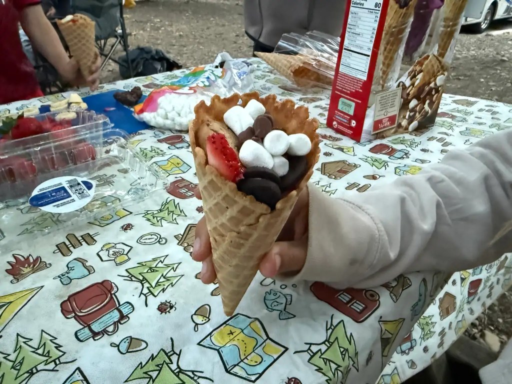 A handing holding an ice cream cone full of marshmallows and cookies to enjoy as a camping dessert.