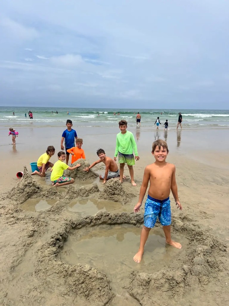 A group of children playing at La Jolla Shores beach in San Diego, building sandcastles and enjoying the water, with waves in the background.