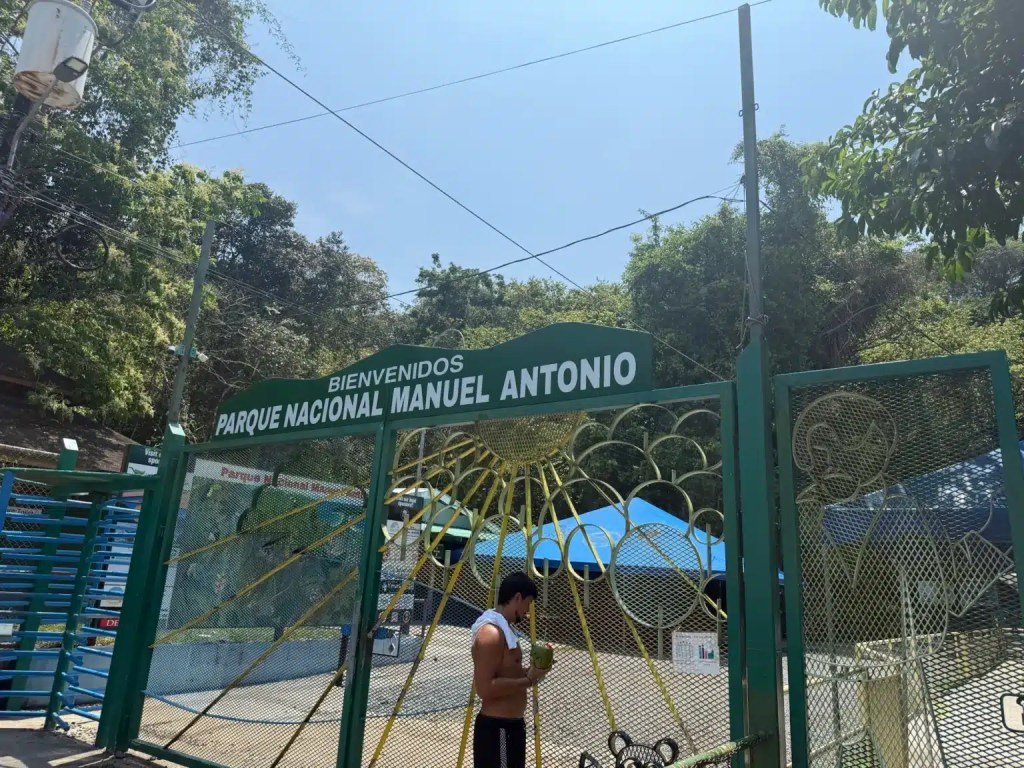 Entrance gate of Parque Nacional Manuel Antonio with a sign welcoming visitors, surrounded by lush greenery.