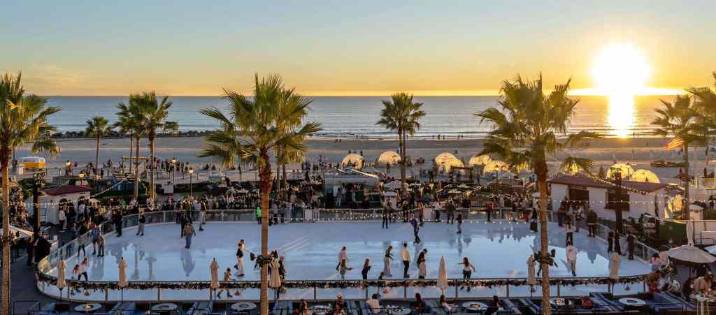An outdoor ice skating rink filled with skaters at sunset, surrounded by palm trees and ocean views at the Hotel del Coronado in San Diego.