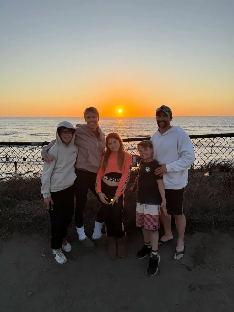 A family posing for a photo at sunset on a beach in San Diego during the winter, with the sun setting over the ocean in the background.