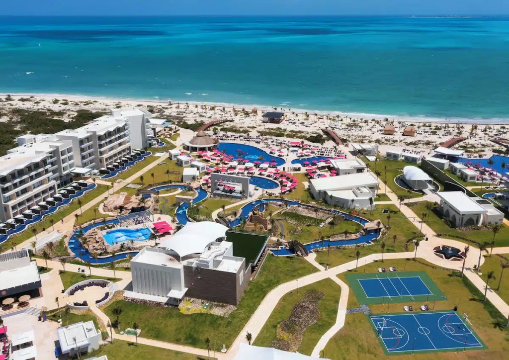 Aerial view of a resort featuring swimming pools, sports courts, and beach access by the turquoise ocean. It's one of the best all inclusive resorts to visit with teens.