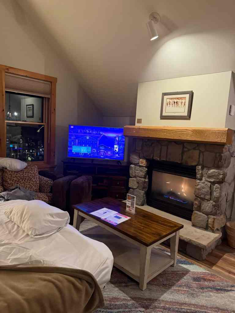 Cozy living room with a fireplace and a TV, featuring a wooden table and plush seating. This is at one of the hotels near Keystone resort.