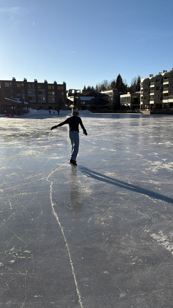 A person skating on an outdoor ice rink in Keystone, Colorado, under a clear blue sky, with buildings and trees in the background.