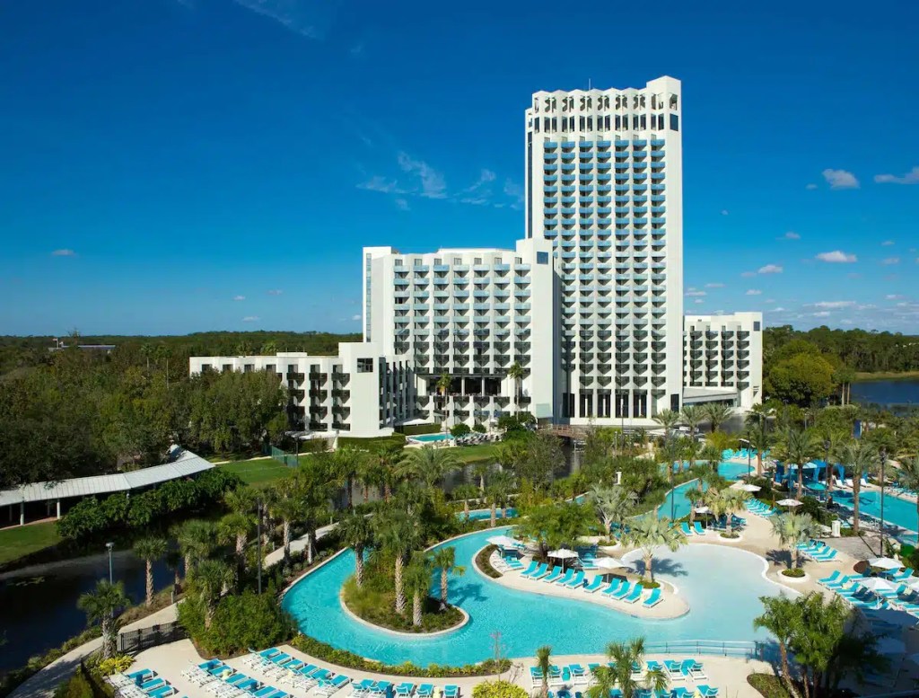 A luxury Orlando resort hotel with a modern design, featuring a large pool area with lazy river surrounded by palm trees and lounge chairs, set against a clear blue sky.