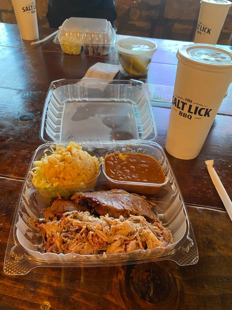 A plate of meat, corn mash and beans with a cup that says Salt Lick BBQ in Texas