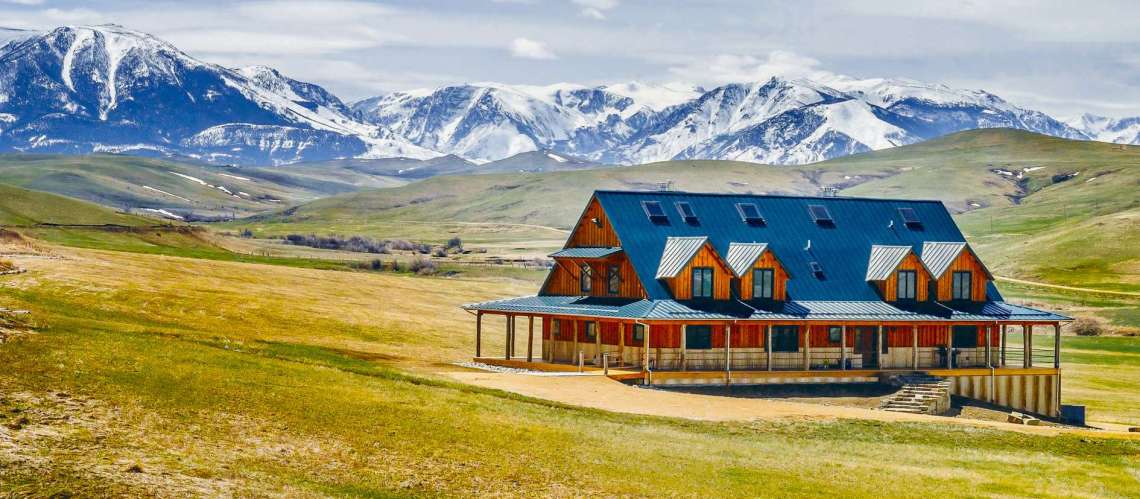 Large wooden all inclusive dude ranch in a wide grassy field with snow-capped mountains in the background