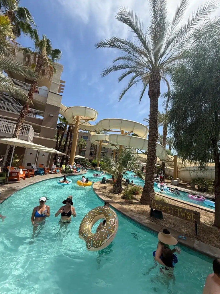 A waterslide and palm tree with people floating in lazy river at one of the waterpark hotels in Palm Springs.