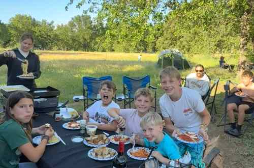 Children eat spaghetti at a picnic table while camping in a grassy field at a campground in Malibu.