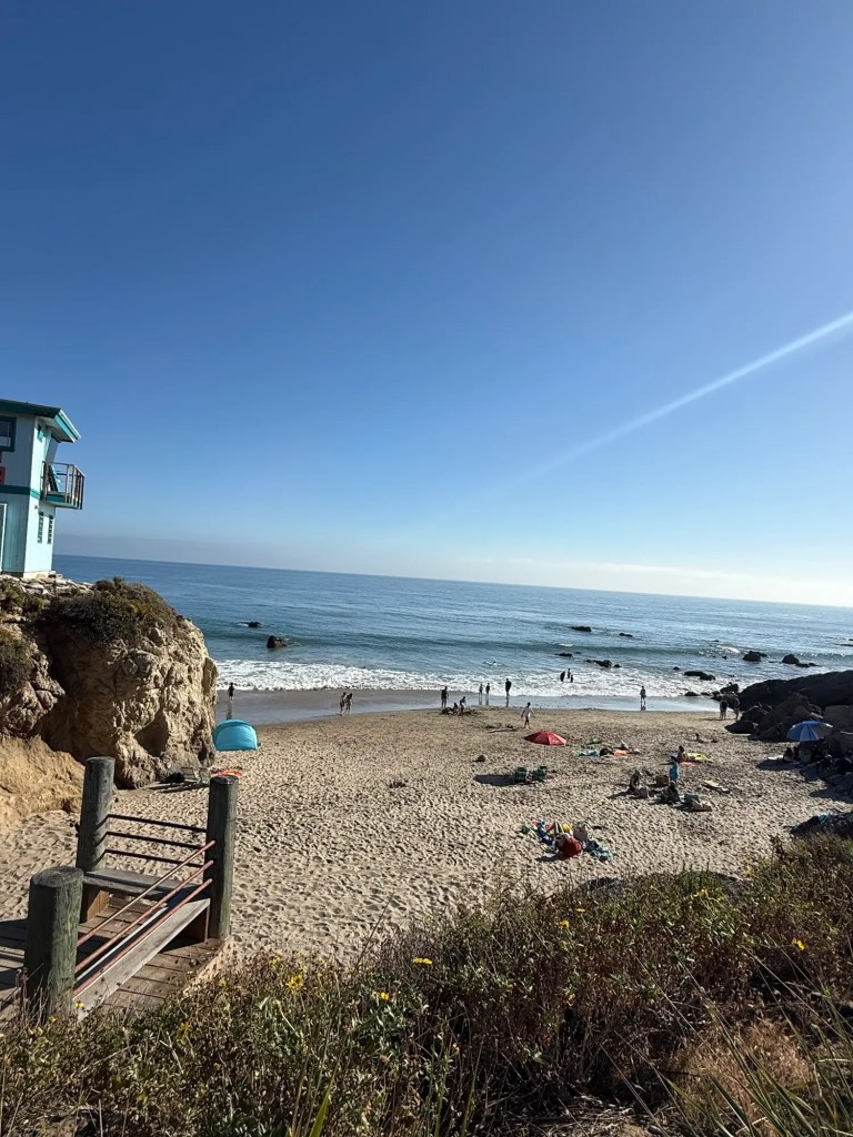 img_2957 A sunny beach with people, ocean waves, and a blue lifeguard tower on a cliff just across from the Leo Carrillo campground.
