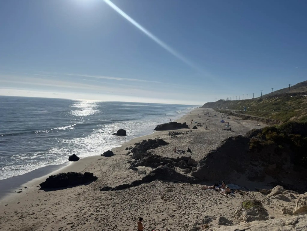 img_2973 Sunny beach with dark rocks and ocean waves under a bright sky with sun flare across from the Leo Carrillo campground.