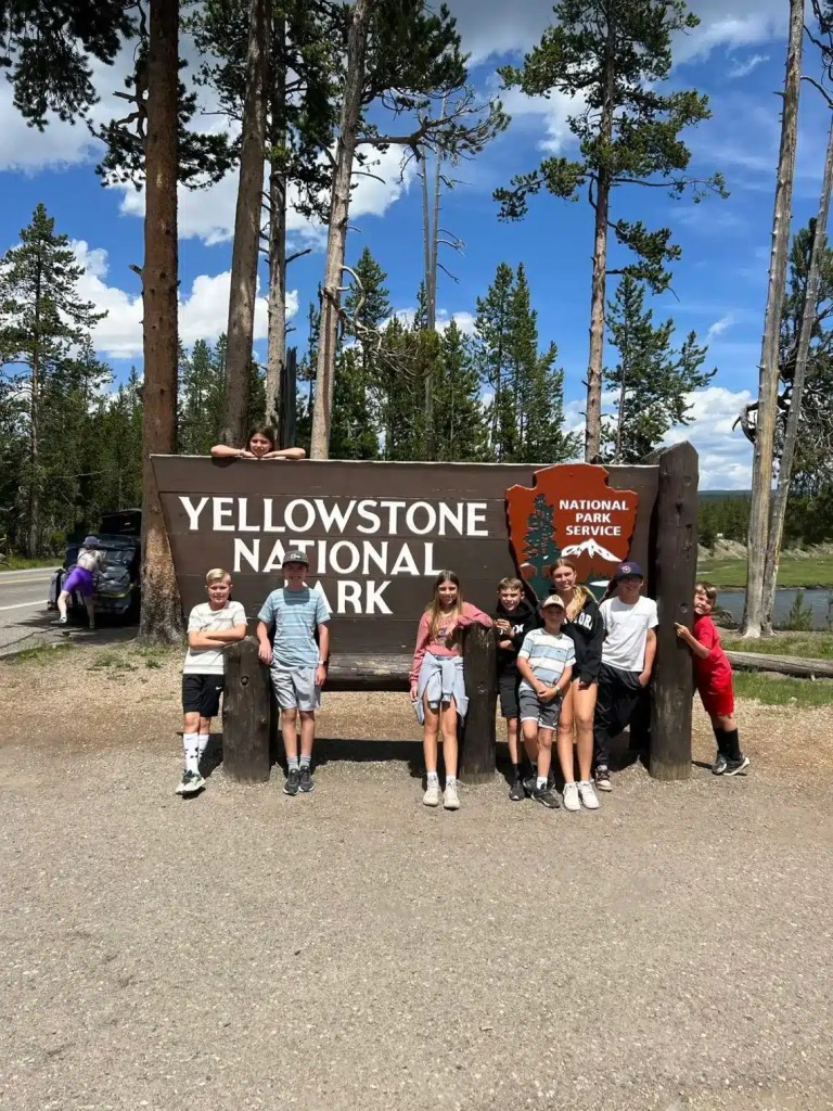 A group of kids posing in front of the Yellowstone National Park sign during their summer break