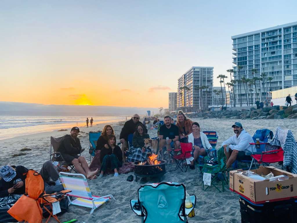 People smiling while having a fire on the sand at one of the best beaches of San Diego