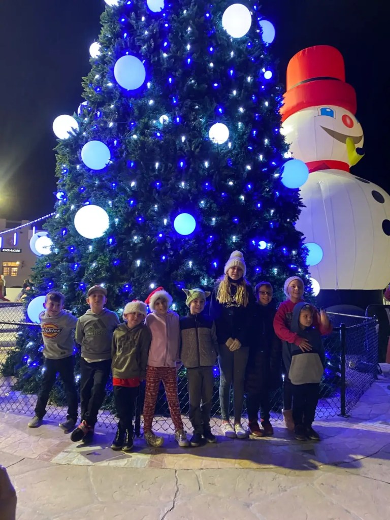 Nine kids with a Christmas tree and snowman in one of the great places to go for Christmas