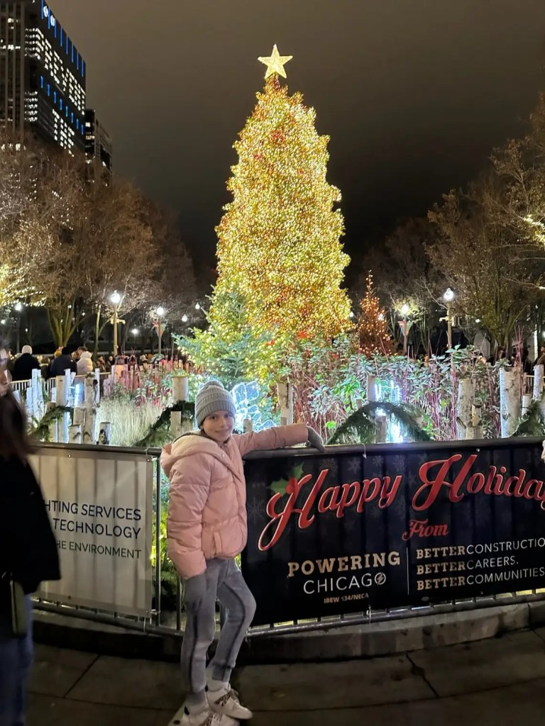 A girl with ice skates in front of a Christmas tree in one of the great places to go for Christmas