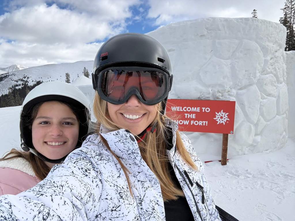A mom and daughter standing in front of a snow fort at one of the best snow resorts