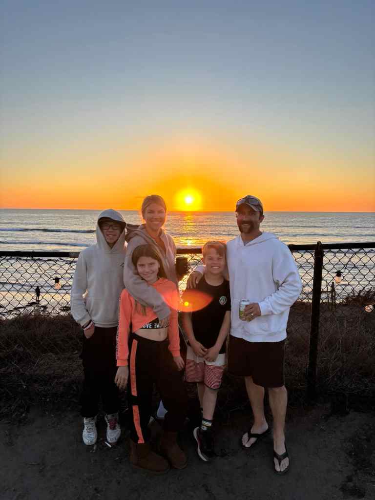A family with a beach sunset behind them at one of the best beaches in Southern California