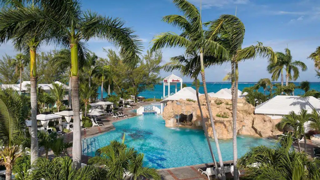 A pool with palm trees and the beach in the background at one of the best family beach resorts