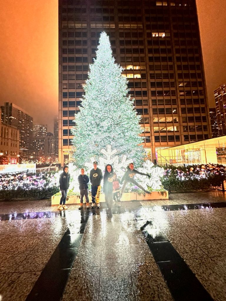 Kids posing with a lit-up Christmas tree while on a Christmas holiday vacation